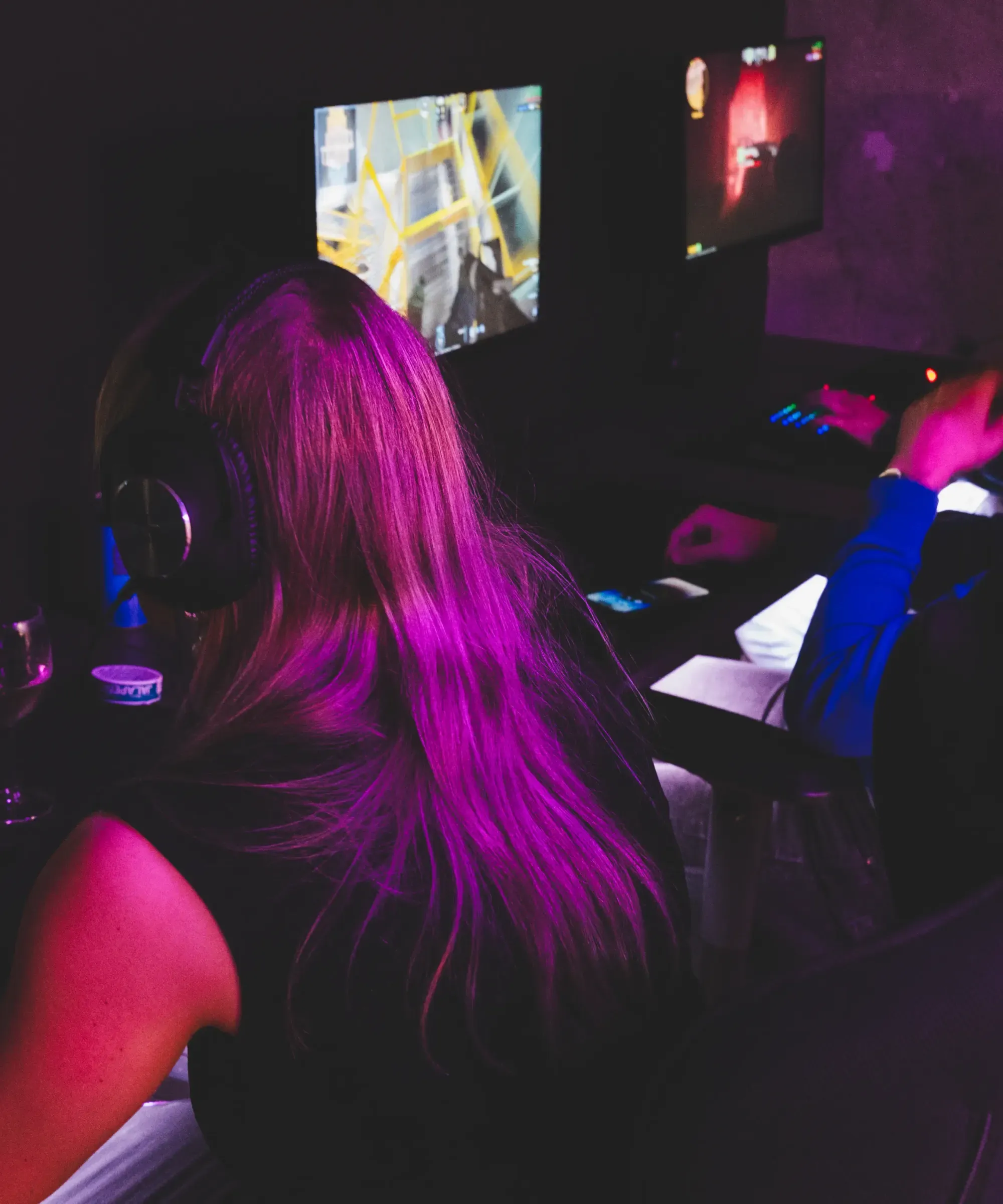 Kollega med headset spelar vid en av gamingriggarna i ett mörkt, lila-upplyst rum