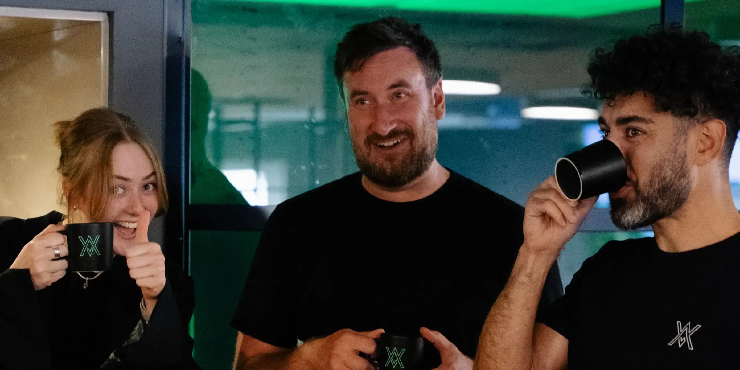 Tre kollegor med Weapp-muggar, en av dem tar en klunk kaffe